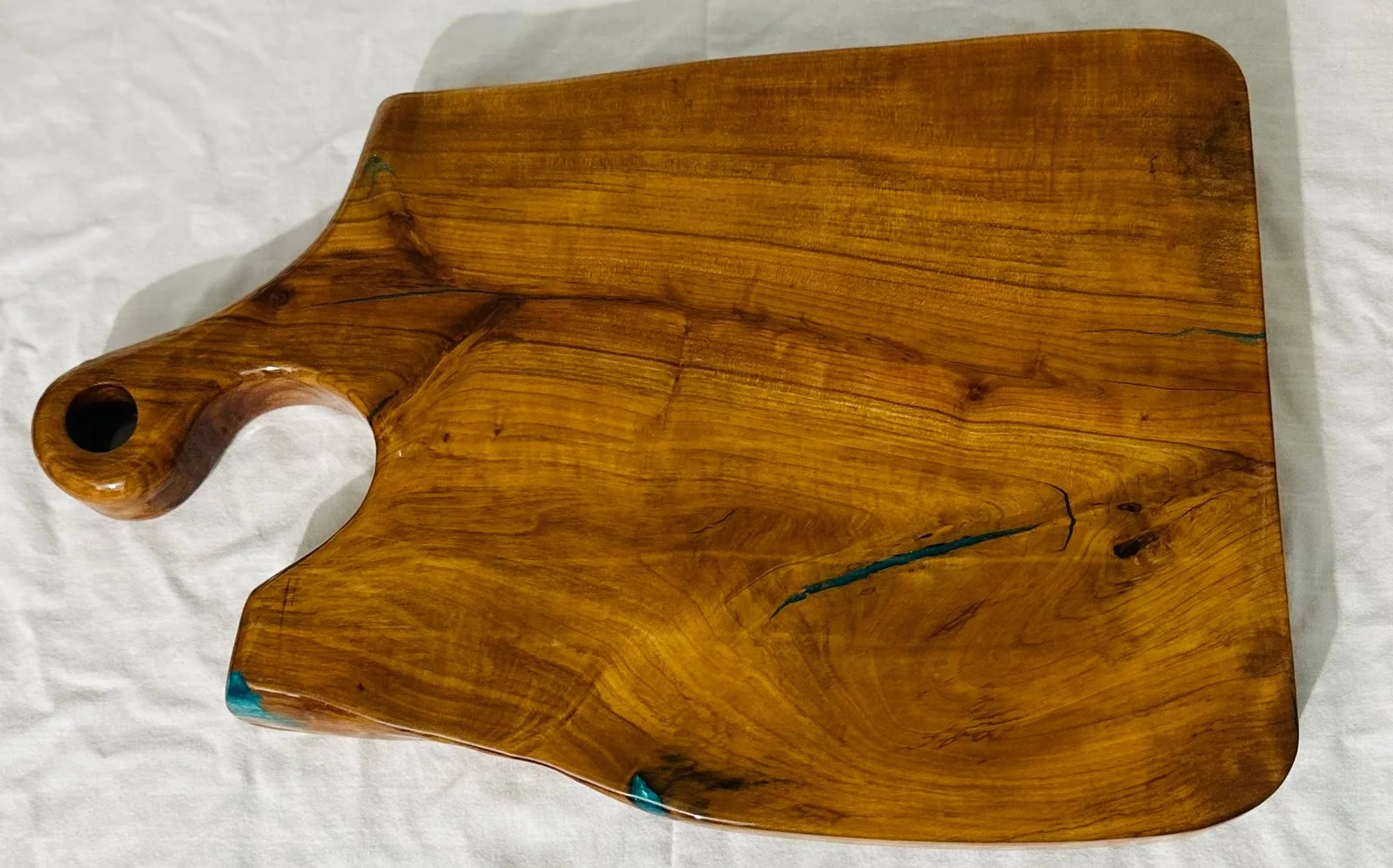 Wide wooden charcuterie board with a sculpted handle and small blue epoxy details