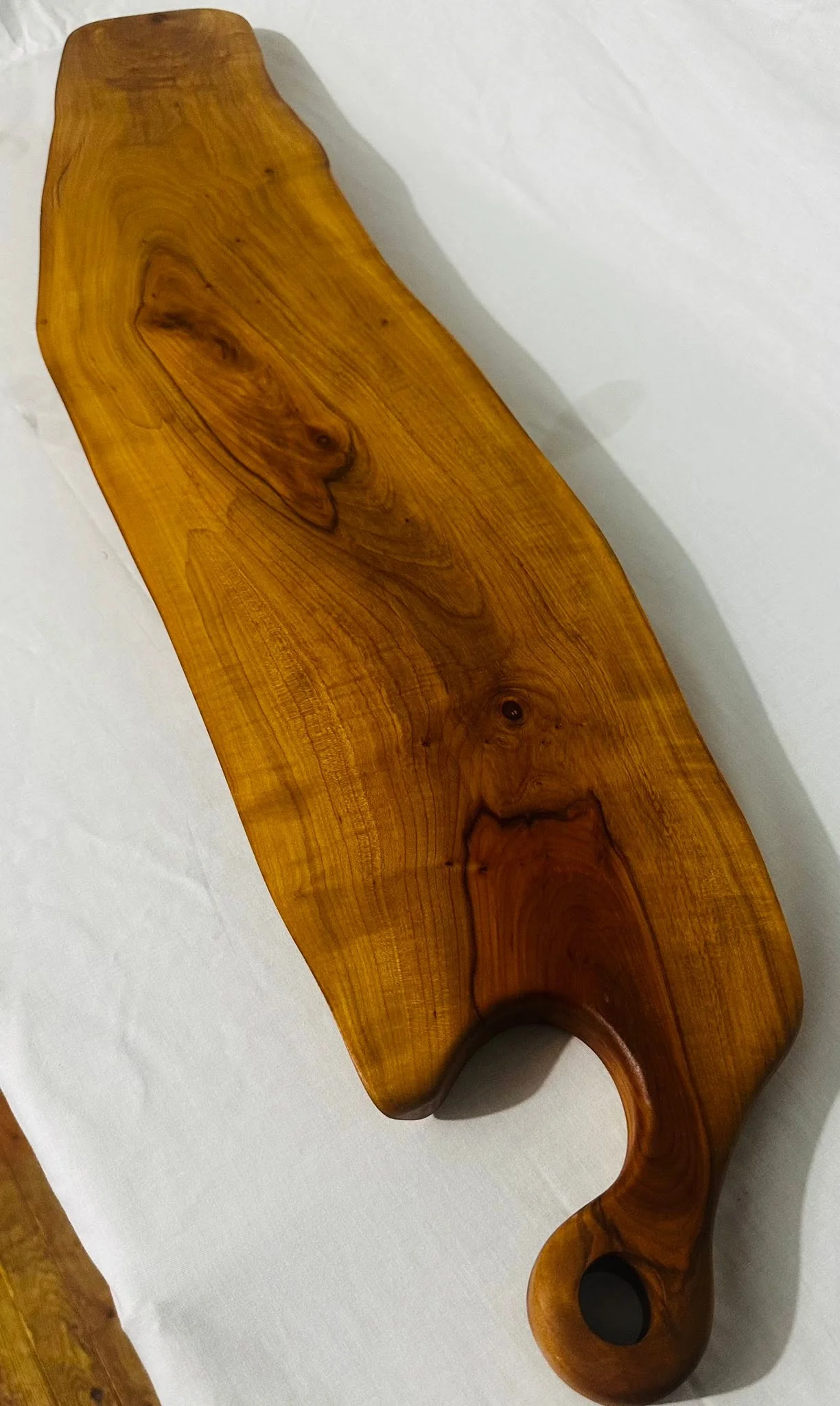 Long wooden serving board with a curved handle and hanging hole